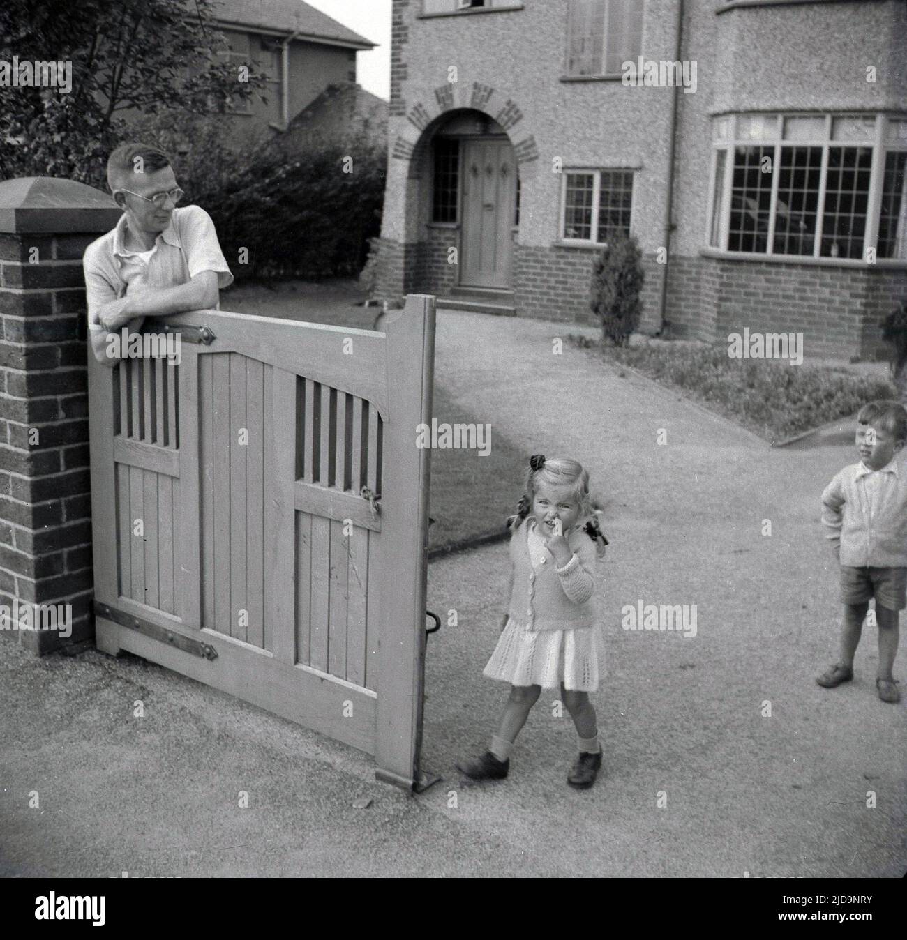 1940s, historical, a father with his two young children at the wooden gate at the entrance drive to their house on Woodford Rd, in the village of Bramhall, a prosperous suburb of Stockport, Cheadle, England, UK. Stock Photo