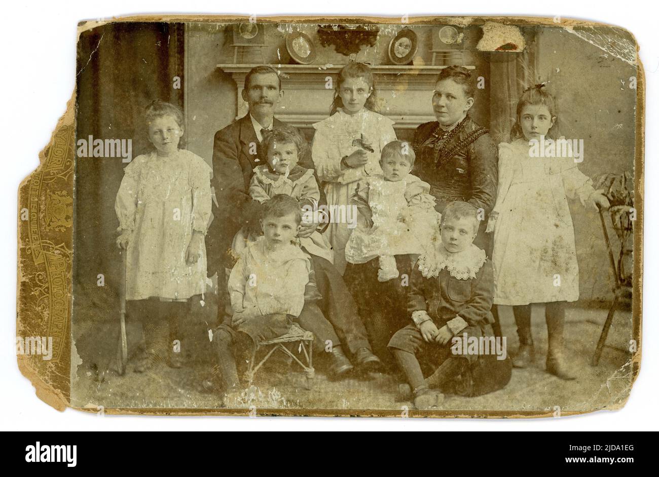 Original, charming, distressed, shabby chic Victorian cabinet card attractive large middle class family, 7 children, mantlepiece in a parlour prop, boys wearing Little Lord Fauntleroy suits. From the studio of  Taylor Photographers, circa 1888, 1889. U.K. Stock Photo