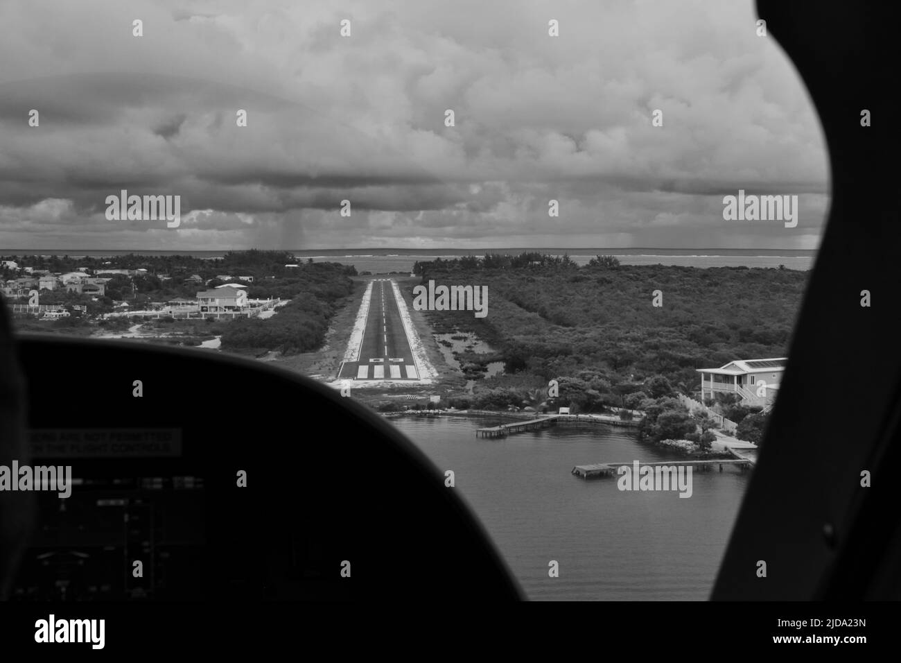 A black and white shot of the runway at the Caye Caulker airport as seen from the cockpit on a cloudy day. Stock Photo