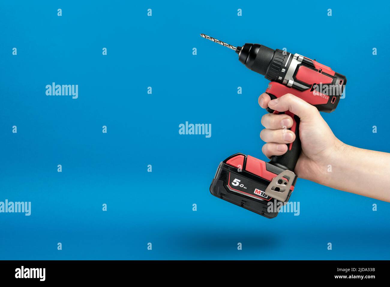 Cordless screwdriver in hand. Cordless tool in a man's hand. The concept of repair and construction on a blue background. Stock Photo