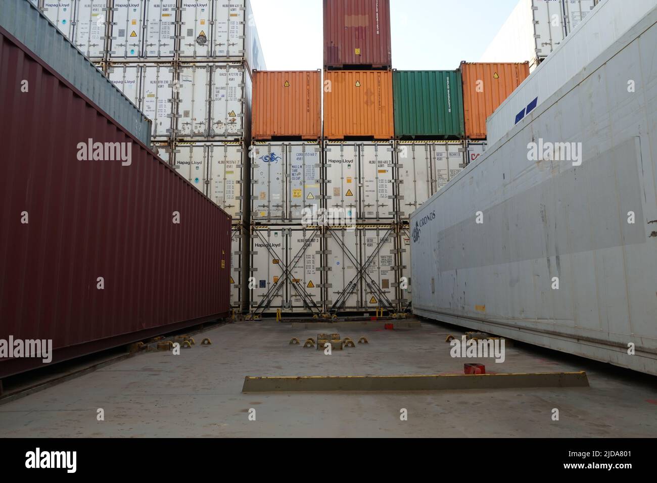 Stowed white reefers and dry cargo containers from different shippers secured on hatch covers of the ship and lashes with lashing bars, turnbuckles Stock Photo