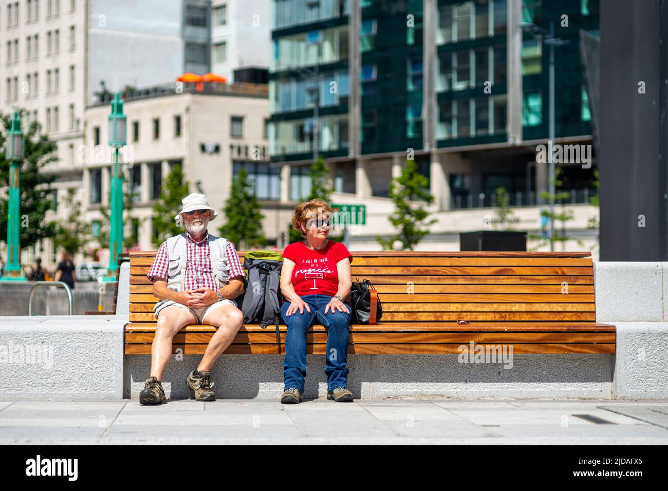 Candid photograph of man and woman couple sitting on a bench in Liverpool, England, UK on a warm sunny day Stock Photo