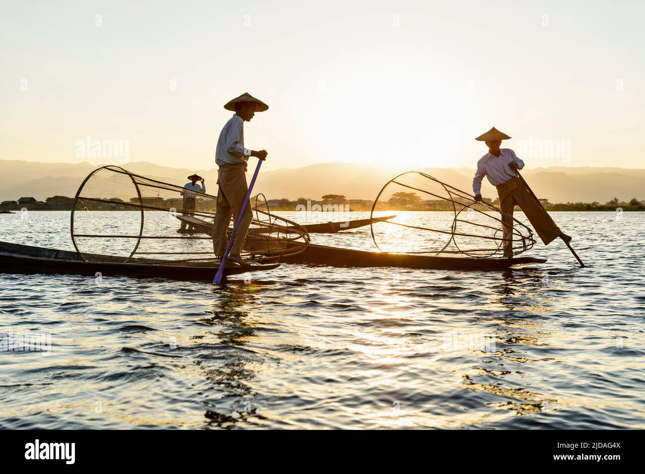 Three fisherman on Inle Lake, standing and using traditional rowing techniques, wrapping a leg around the oar. Stock Photo
