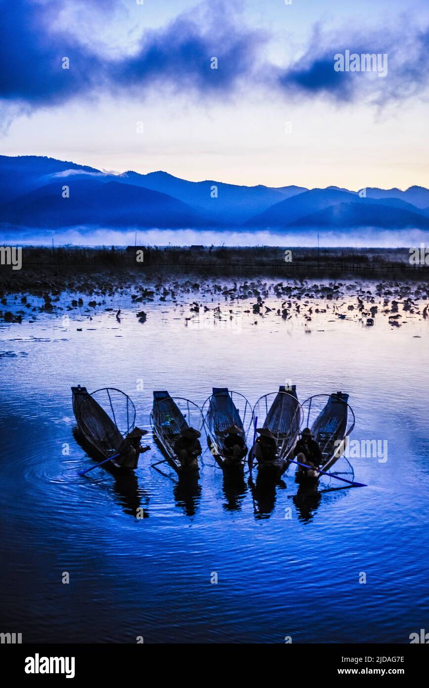A group of fishermen on Lake Inle at dusk, mist rising from the water. Stock Photo