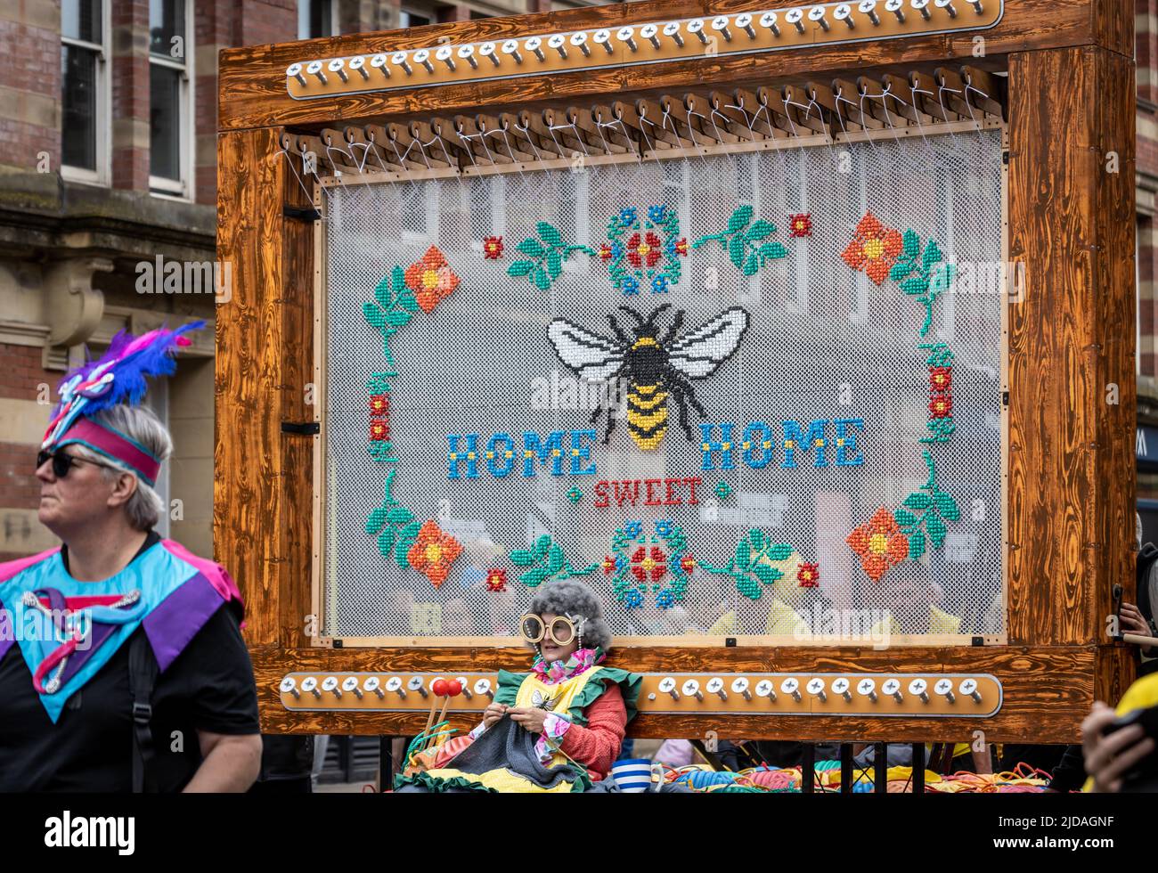Manchester Day Parade, 19 June 2022: Lady knitting underneath a 'Home sweet home' tapestry Stock Photo