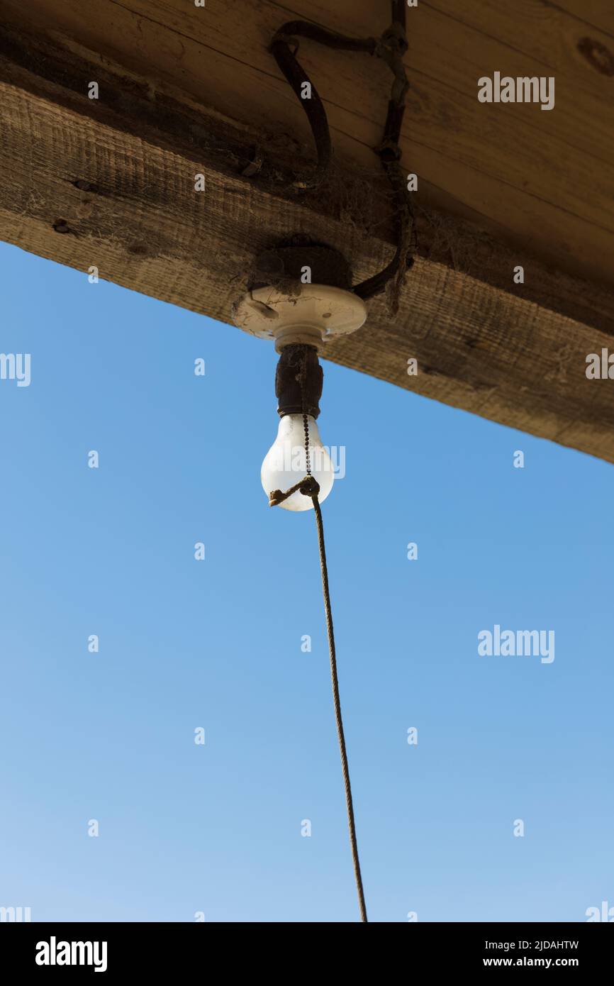 Old incandescent light bulb on a porch beam with a string pull control Stock Photo