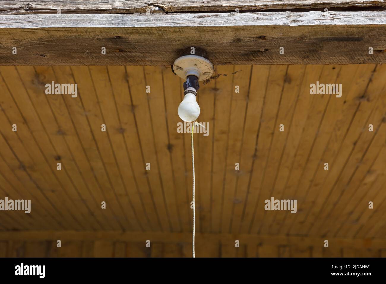 Old incandescent light bulb on a porch beam with a string pull control Stock Photo