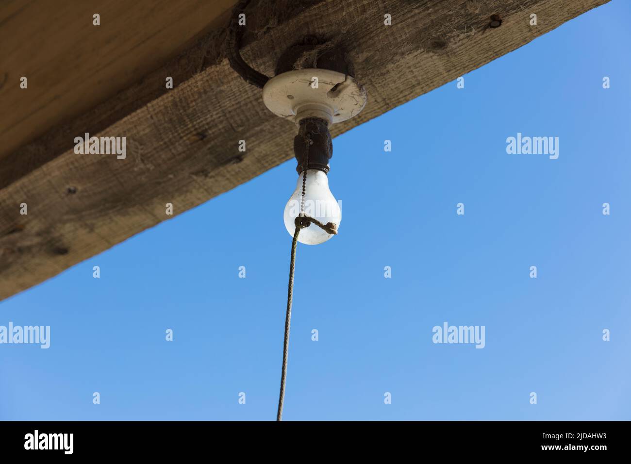 Old incandescent light bulb on a porch beam with a string pull control. Stock Photo