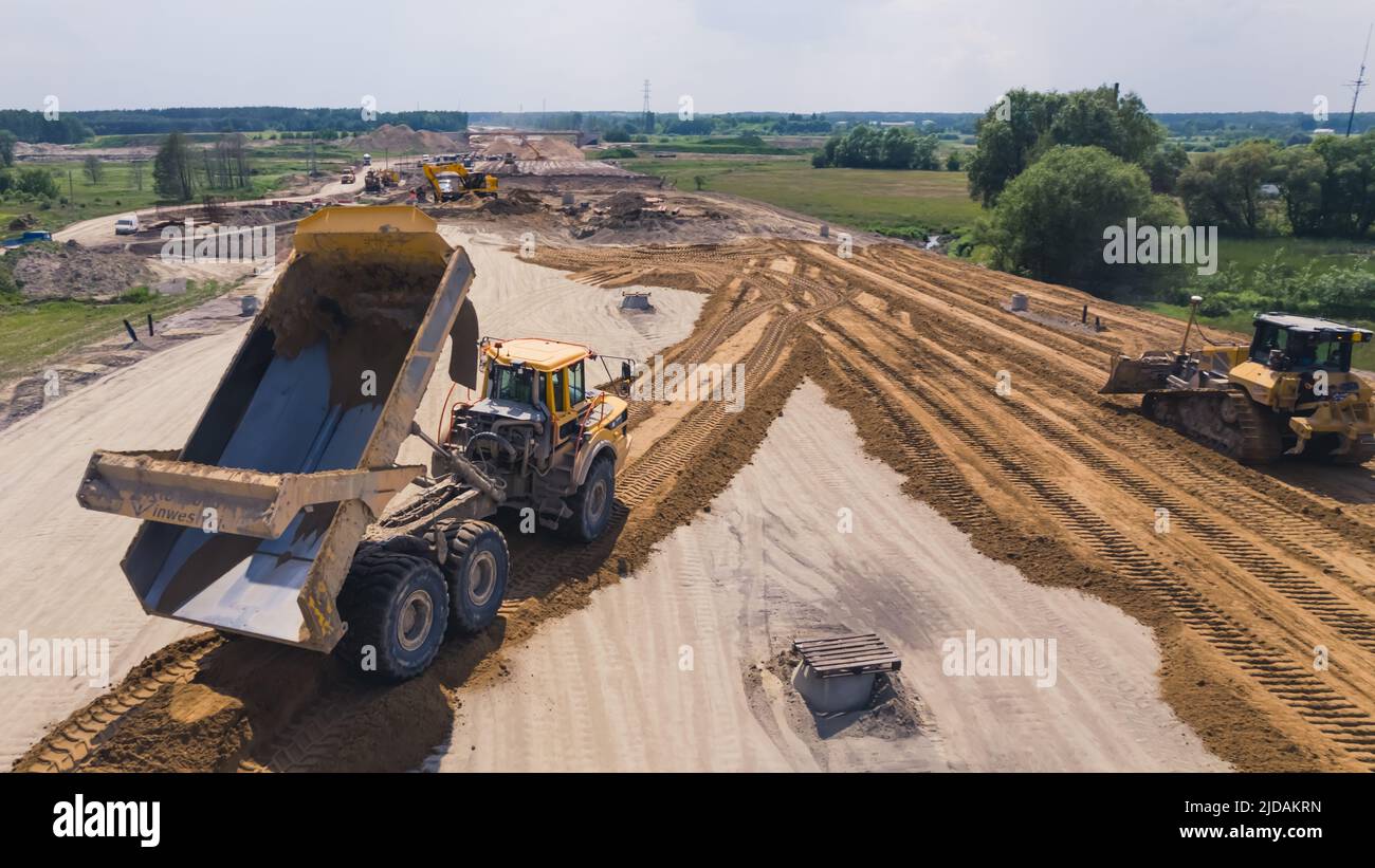 A yellow and black industrial machine spreading loose sand at a road