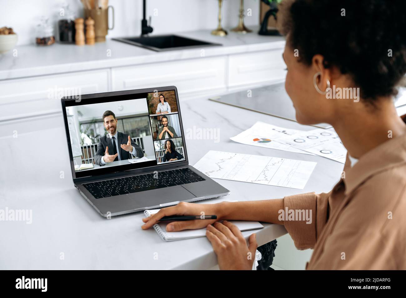 Over shoulder view of African American girl of laptop screen with multiracial people. Female brainstorming with work colleagues, listening to online webinar using laptop and video conference Stock Photo