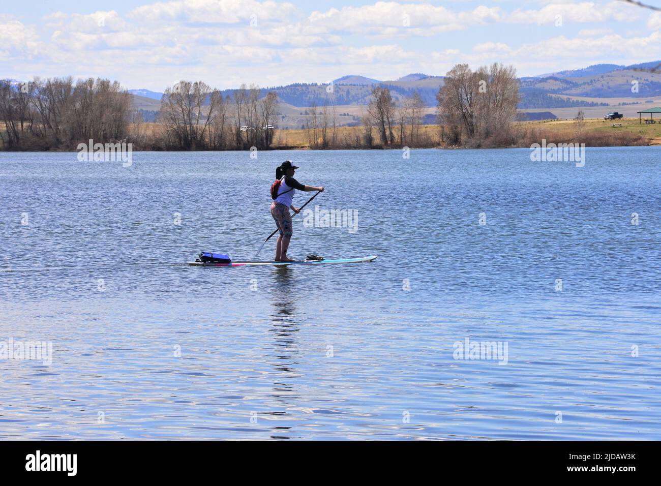 Woman is Paddleboarding on a calm lake with distant mountains and trees