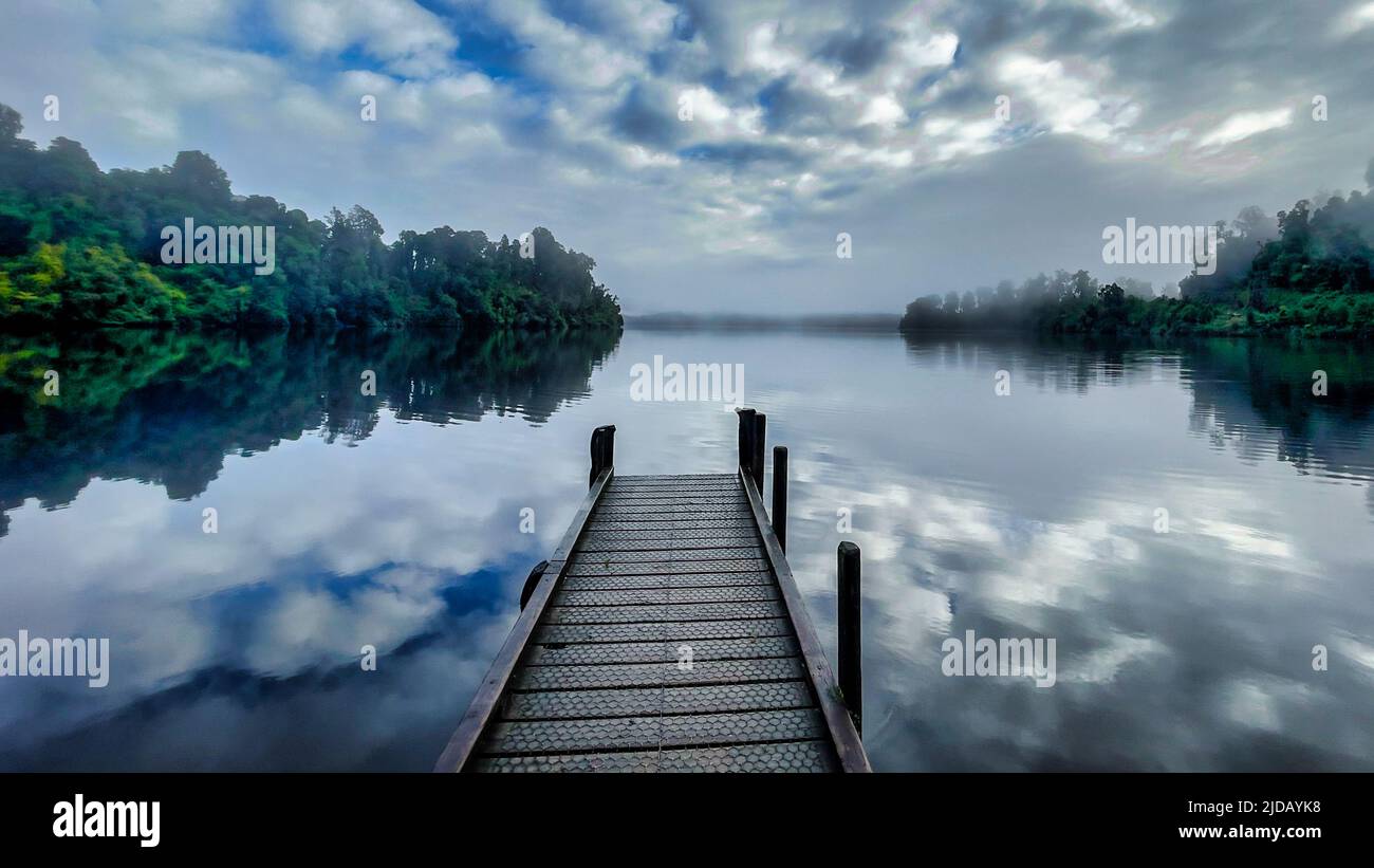 Lake Mapourika on the South Island West Coast with its jetty shrouded in in mist and low cloud in the early morning Stock Photo