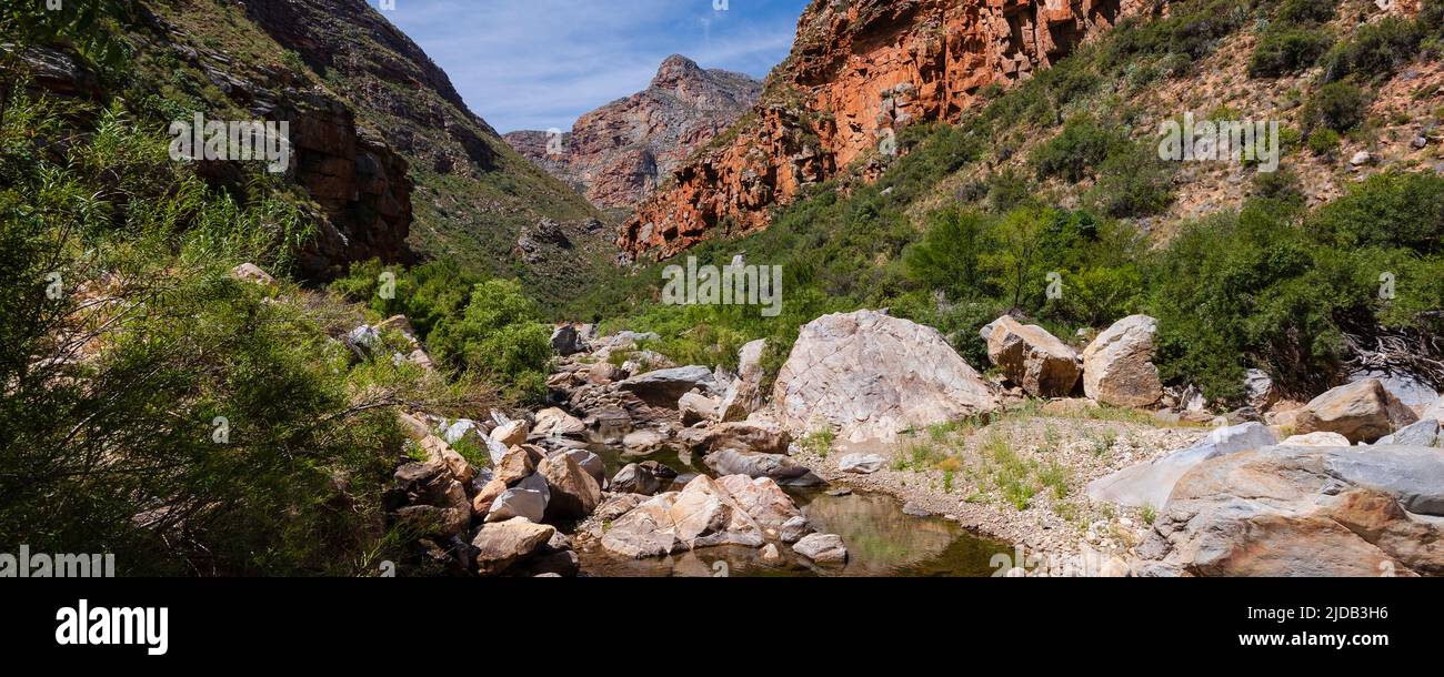 View of a mountain peak through rocky cliffs with a stream surrounded by boulders in the foreground; Western Cape, South Africa Stock Photo