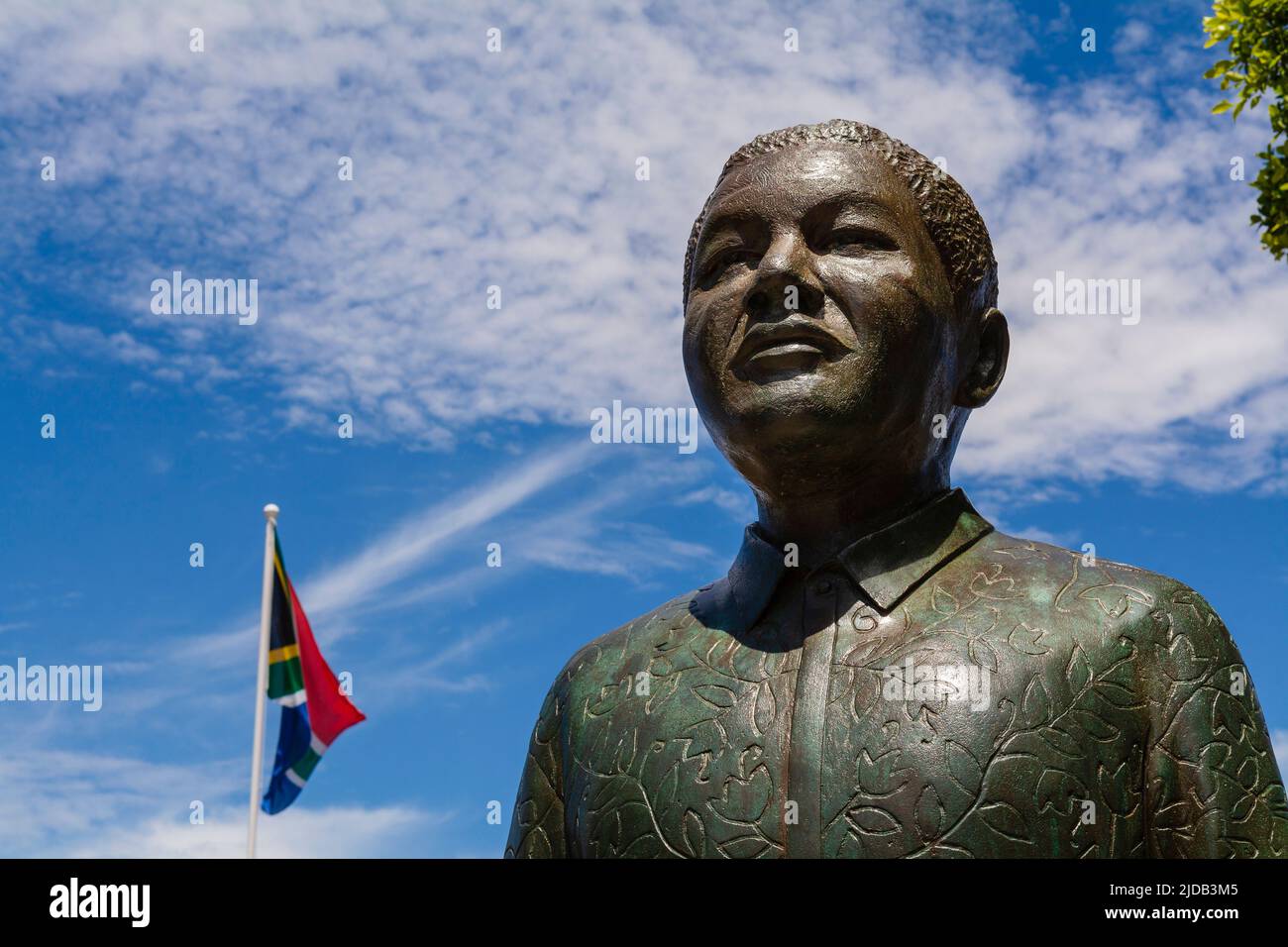 Close-up of the Nelson Mandela bronze statue in Noble Square along the Victoria and Alfred Waterfront with the South African flag flying against a ... Stock Photo