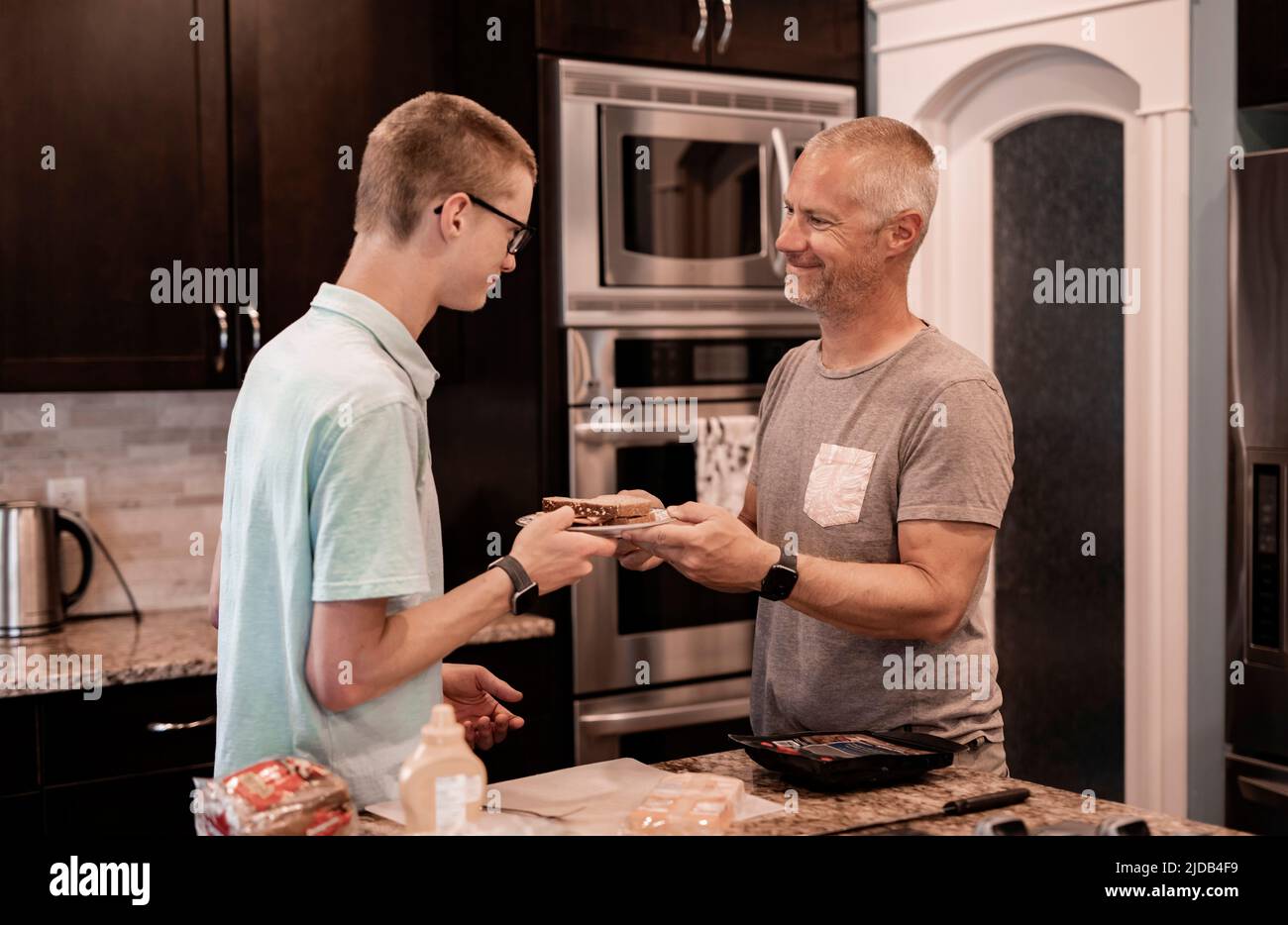 Young man serving his dad a sandwich in the kitchen at home; Edmonton, Alberta, Canada Stock Photo