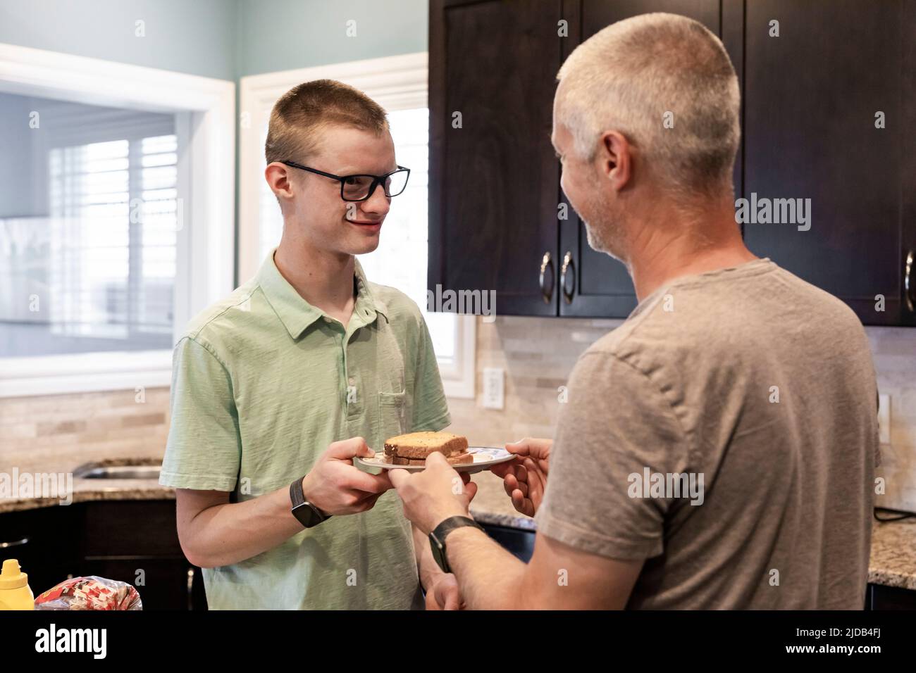 Young man serving his dad a sandwich in the kitchen at home; Edmonton, Alberta, Canada Stock Photo