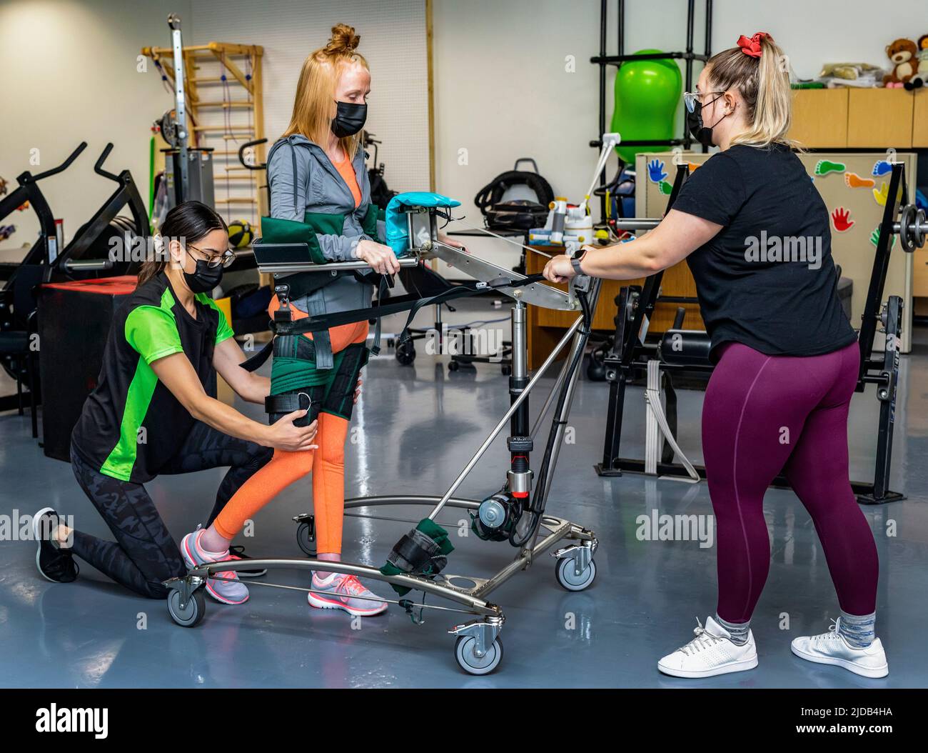 A paraplegic woman working out using an assisted walking machine with her trainers; Edmonton, Alberta, Canada Stock Photo