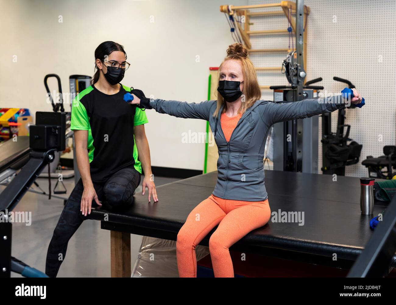 A paraplegic woman doing bilateral raises during her workout wiht her trainer: Edmonton, Alberta, Canada Stock Photo