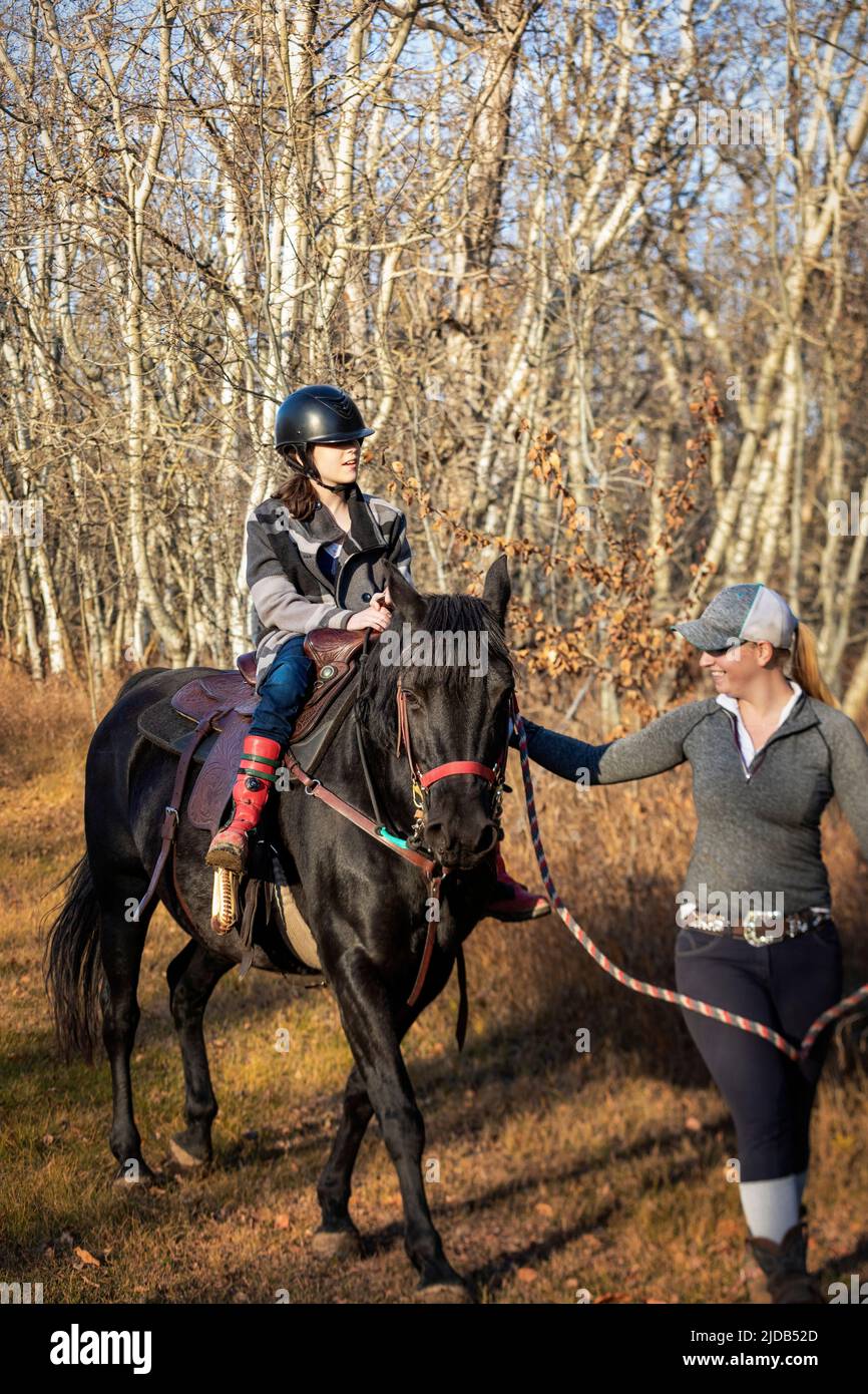 A young girl with Cerebral Palsy and her trainer working with a horse on a trail ride during a Hippotherapy session; Westlock, Alberta, Canada Stock Photo