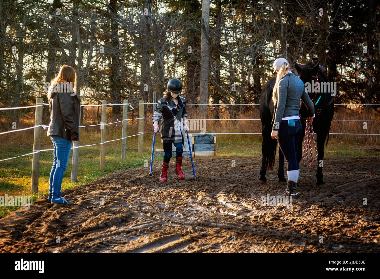 A young girl with Cerebral Palsy finishes up her Hippotherapy session with her Mom and her trainer who is leading the horse; Westlock, Alberta, Canada Stock Photo