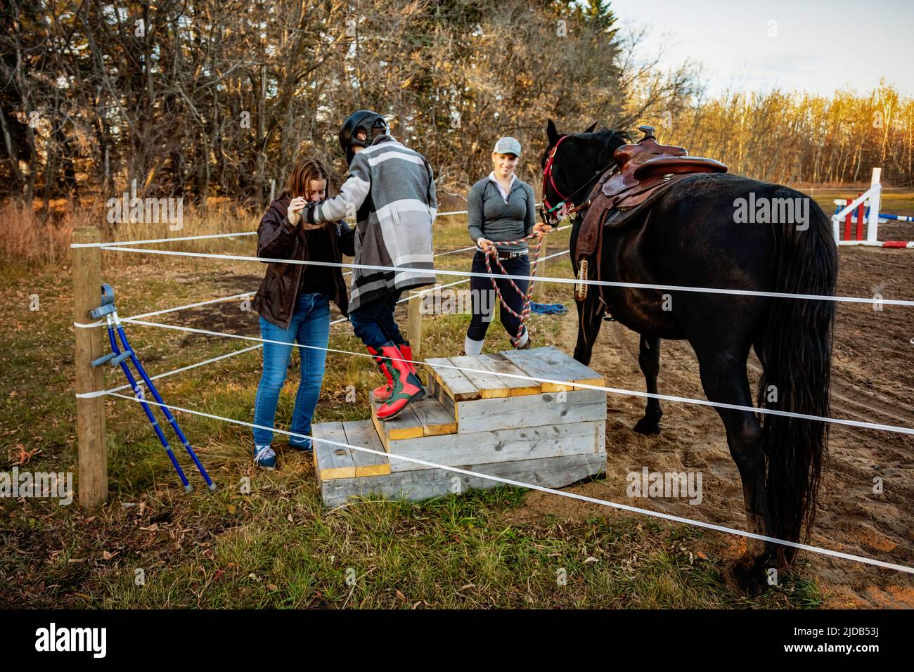 A young girl with Cerebral Palsy getting off her horse during a Hippotherapy session with the help of her mom and her trainer Stock Photo