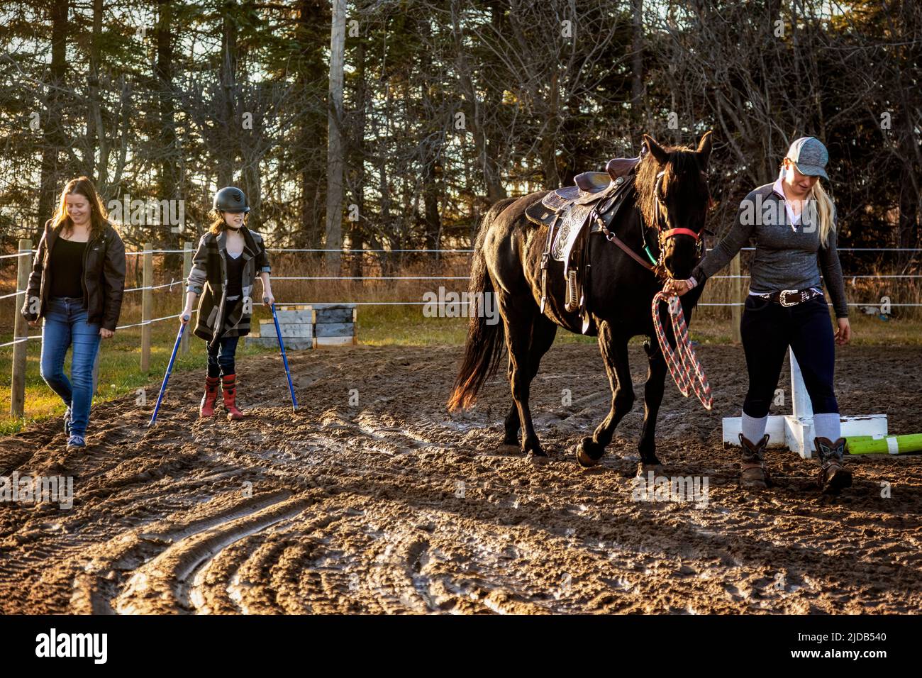 A young girl with Cerebral Palsy finishes up her Hippotherapy session with her Mom and her trainer who is leading the horse; Westlock, Alberta, Canada Stock Photo