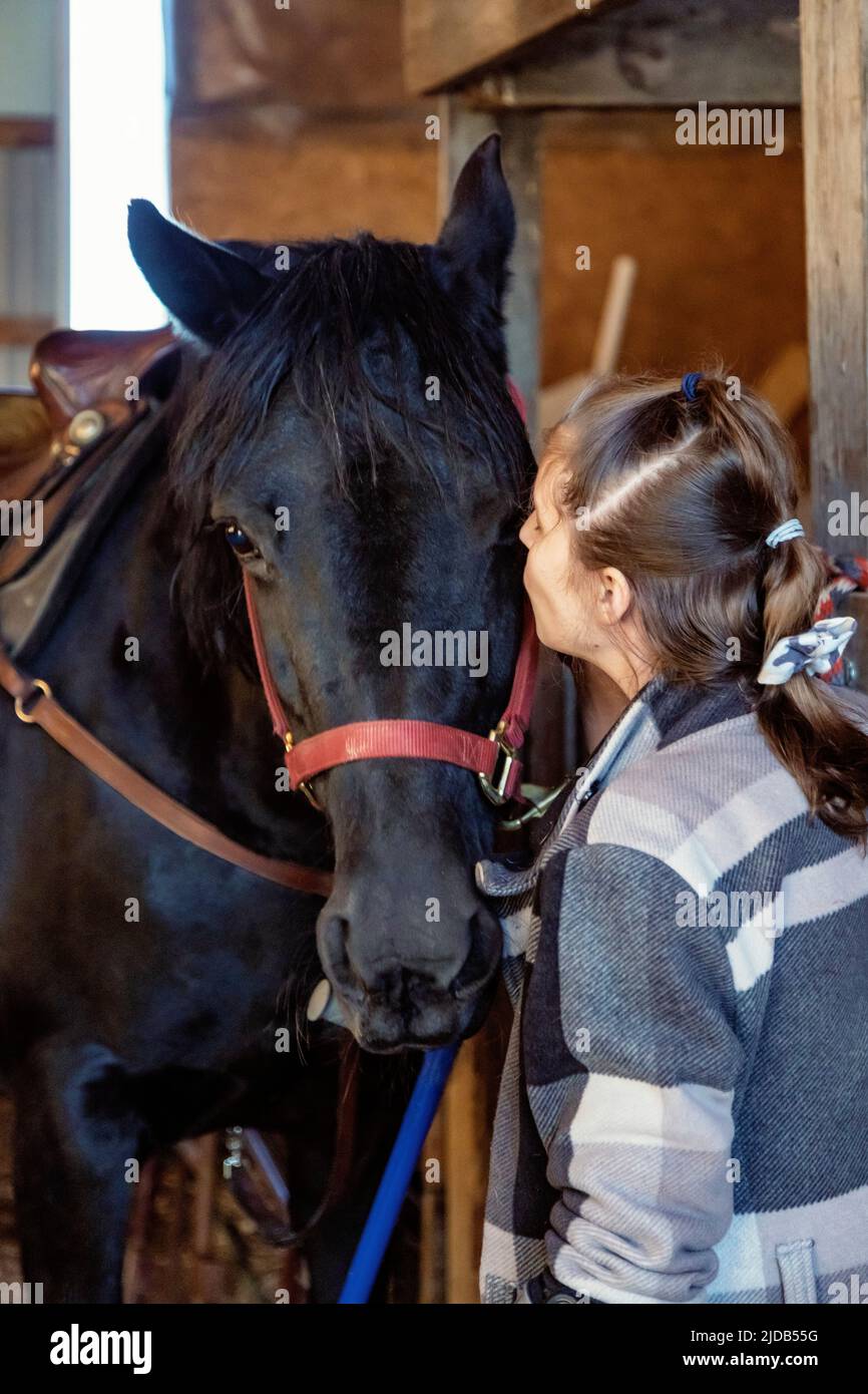 A young girl with Cerebral Palsy kissing a horse in a barn during a Hippotherapy session; Westlock, Alberta, Canada Stock Photo