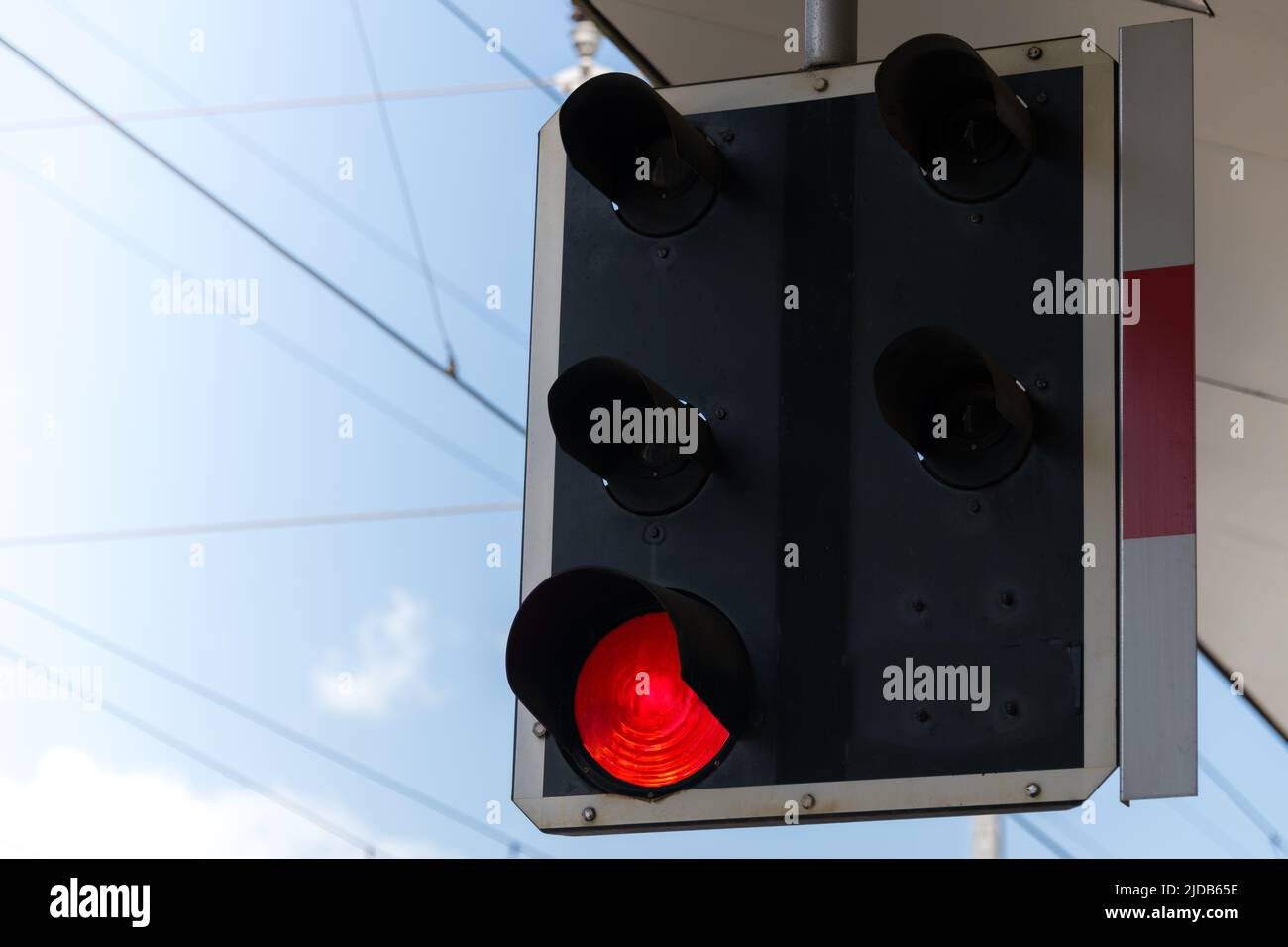 Close up of a railroad signal traffic light with red light on a platform against blue partly