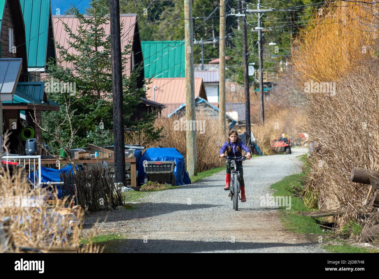 A young girl rides her bike down the pathway in Tenakee Springs, Alaska. Regular motor vehicles are not allowed in the small Southeast village. Stock Photo