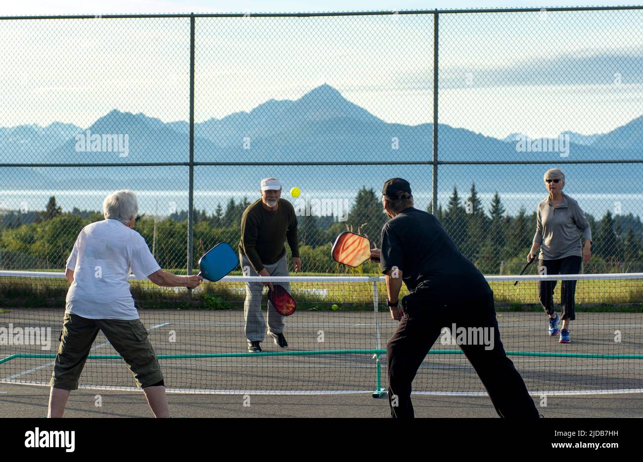 Senior men and women play Pickleball outdoors at the Homer High School with the Kenai Mountains and Kachemak Bay as a backdrop. Stock Photo