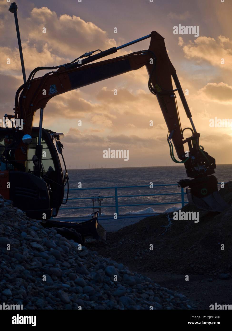Stationary digger at sunset by the sea with mound of stones and earth, Brighton, East Sussex, UK © Renzo Frontoni / Axiom Stock Photo