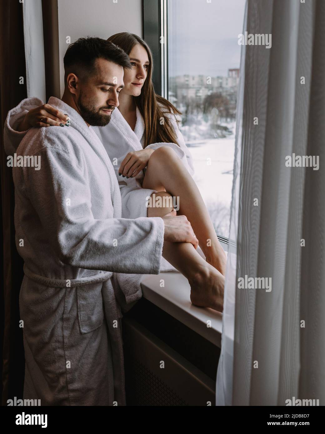 Couple wearing bathrobes in hotel standing near window Stock Photo