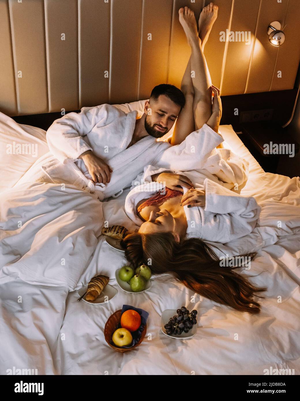 Happy young couple sitting in bed in morning and having breakfast Stock Photo
