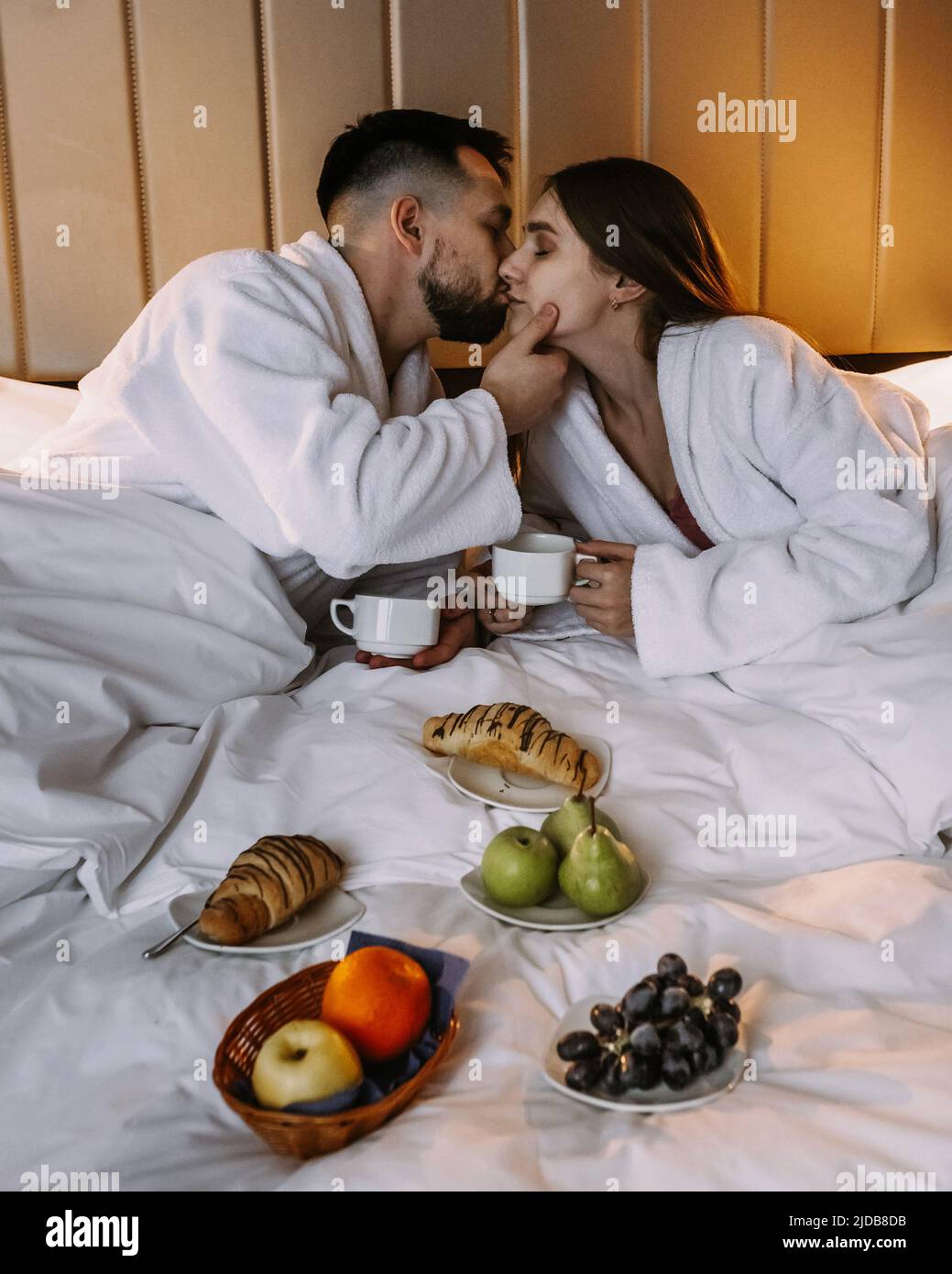 Happy young couple sitting in bed in morning and having breakfast Stock Photo