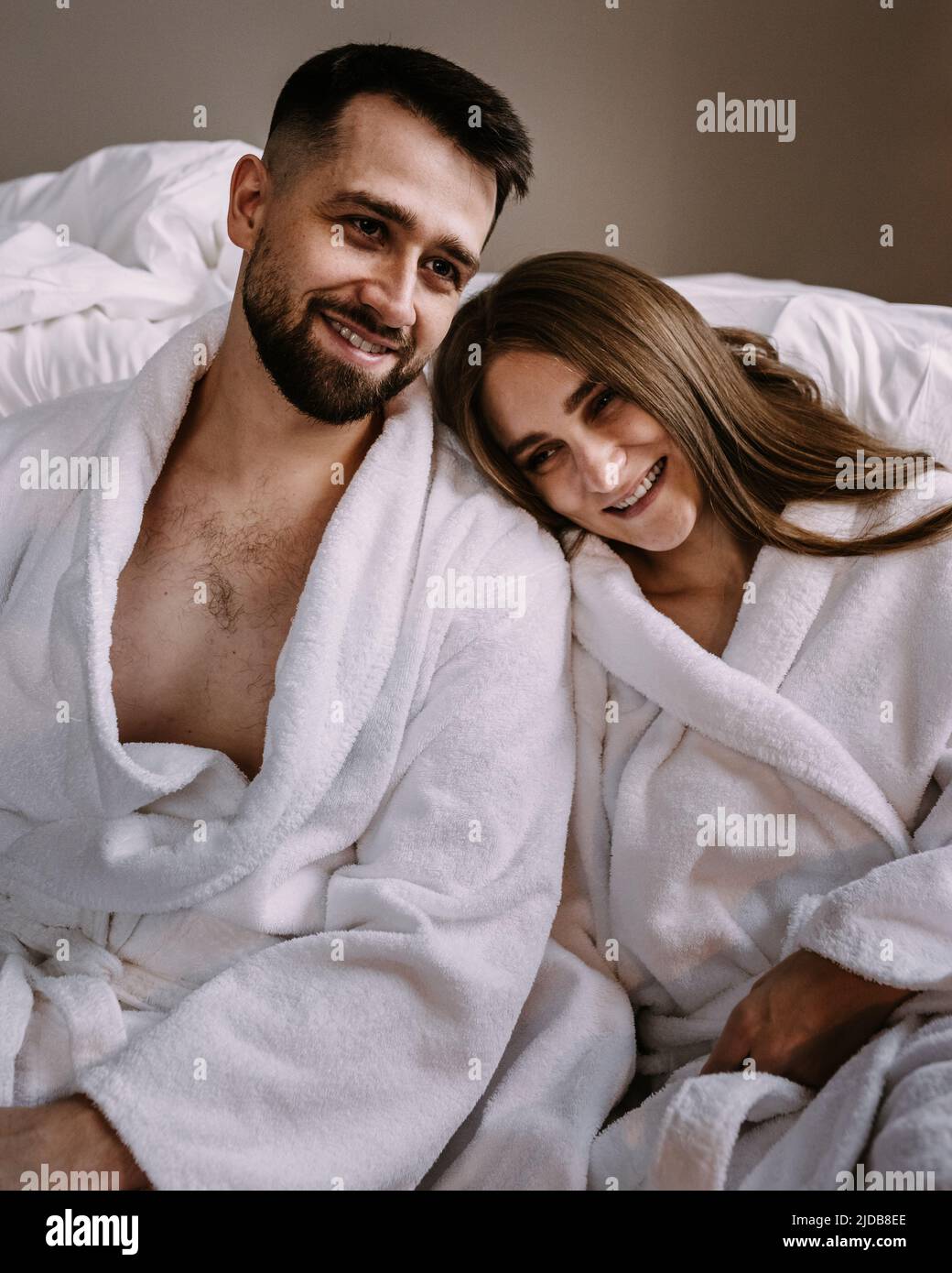 Portrait of happy young couple hugging and kissing sitting on floor near the bed in hotel Stock Photo