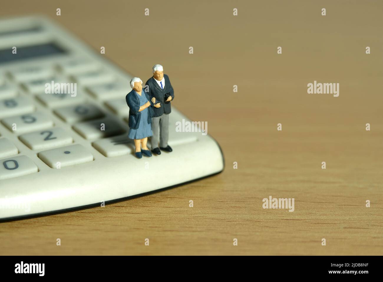 Miniature people toys conceptual photography. Elderly couple standing above calculator. Image photo Stock Photo
