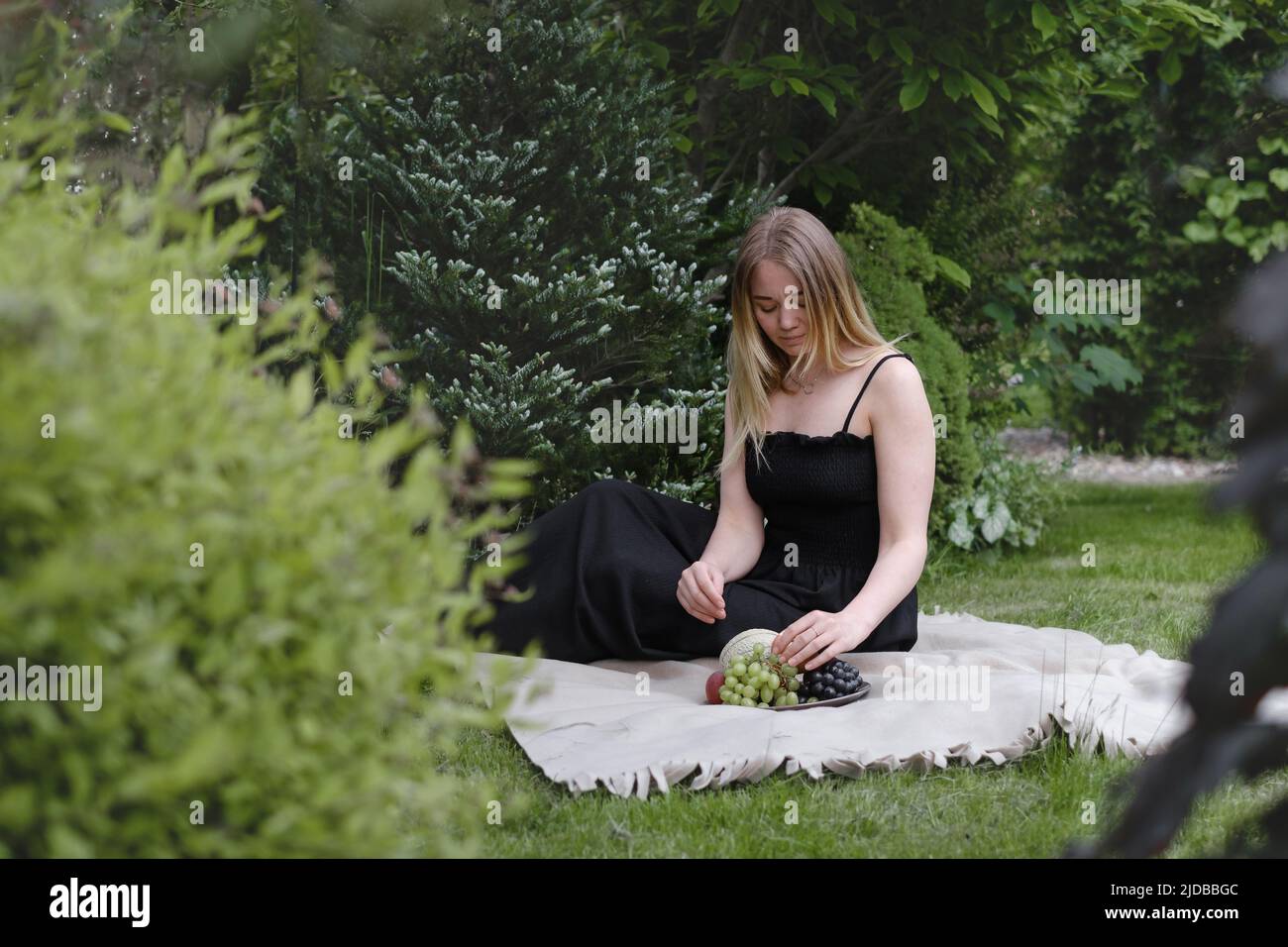 Woman on picnic in green garden On blanket. Cheerfully female spend time outdoors, eating summer fruits. Vegetarian eco idea for weekend picnic Stock Photo