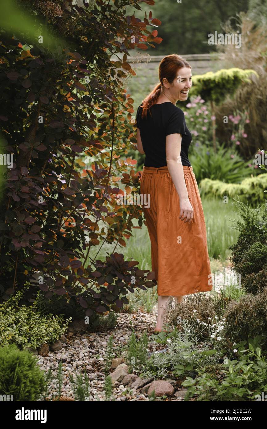 Happy ginger hair woman walking barefoot in the park or garden. Freedom and healthy way of life. Female in her 40s having rest outdoors. People in Stock Photo