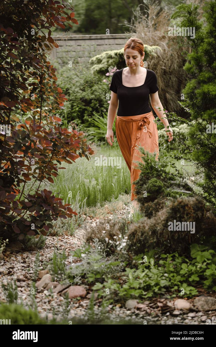 Happy ginger hair woman walking barefoot in the park or garden. Freedom and healthy way of life. Female in her 40s having rest outdoors. People in Stock Photo