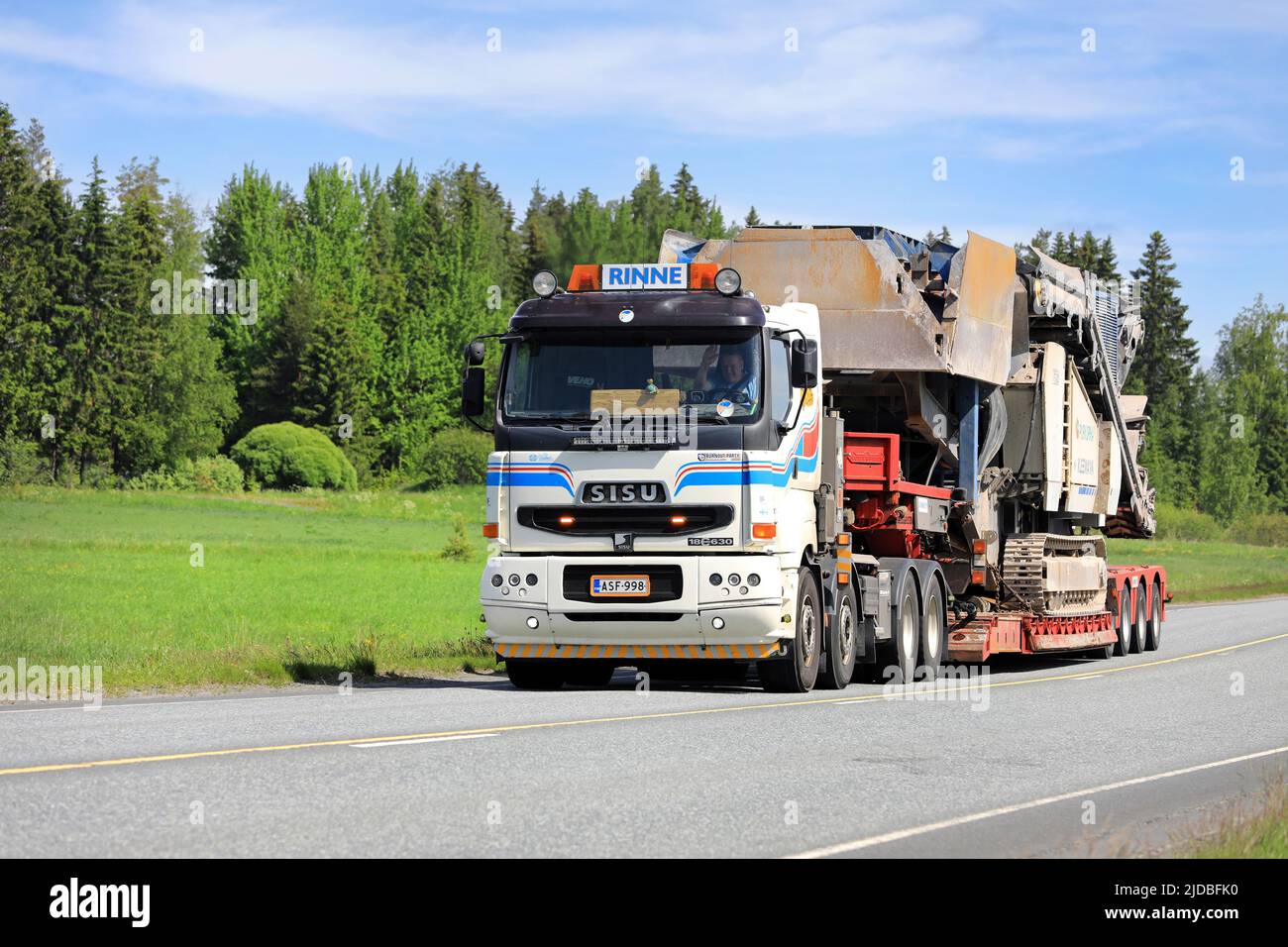 White Sisu 18E630 truck of O.Rinne Oy transports Kleemann crusher on low loader trailer on highway 10 in the summer. Jokioinen, Finland. June 10, 2022 Stock Photo