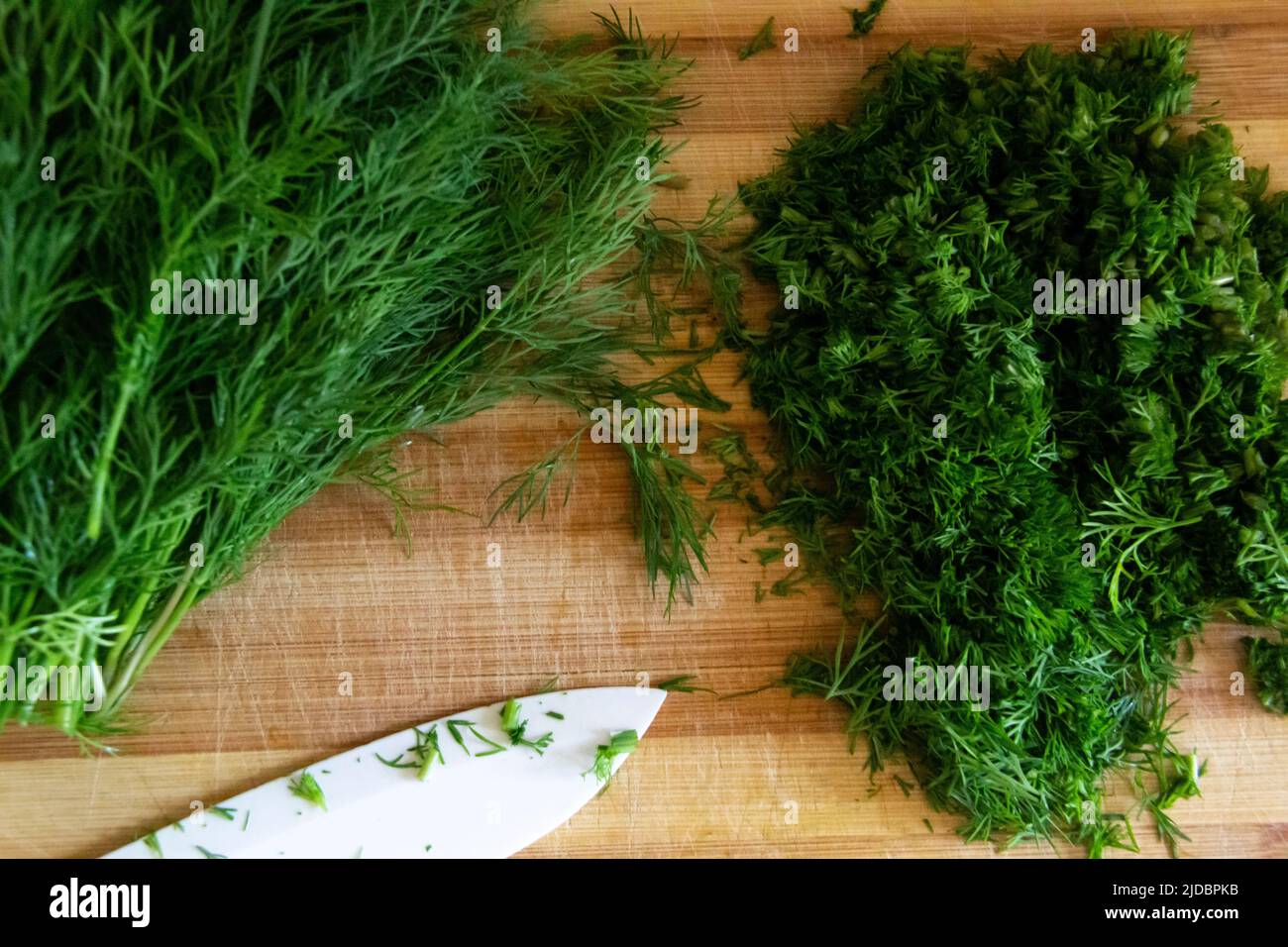 A chopping dill on a board. Homemade preparation of chopped dill with a knife on the wooden board against background. Green seasoning fresh dill on th Stock Photo