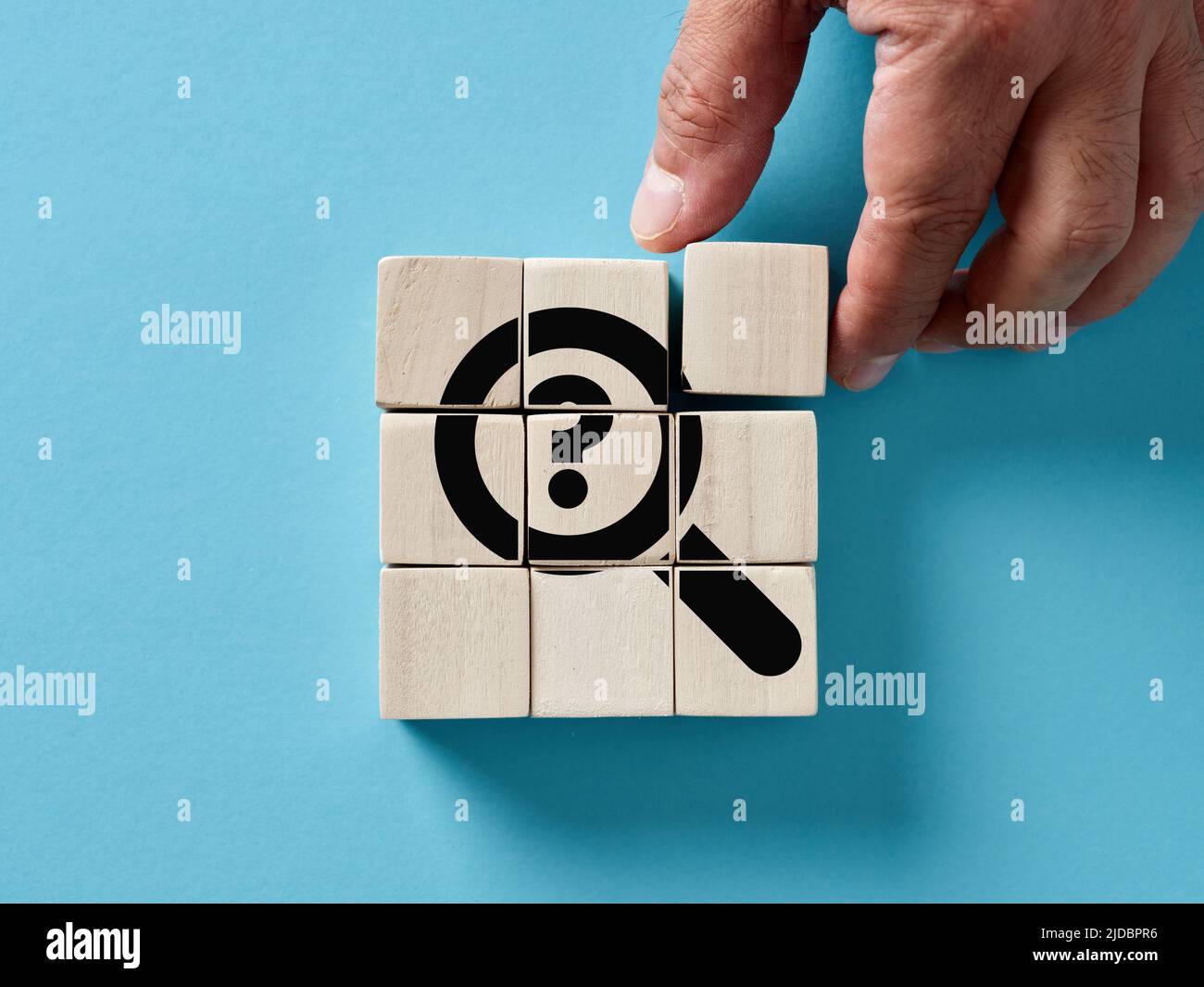 Male hand arranging wooden cubes with a magnifier and question mark ...