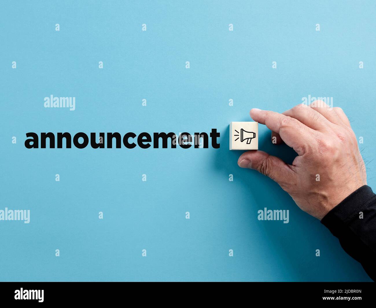 Male hand puts the wooden cube with megaphone symbol next to the word announcement. Important announcement concept. Stock Photo