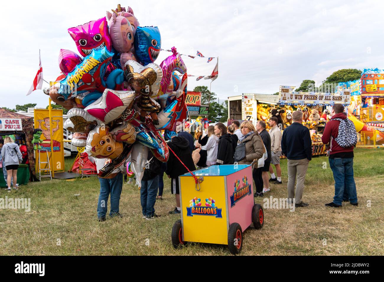 A balloon stall and people spending leisure time at the funfair. The