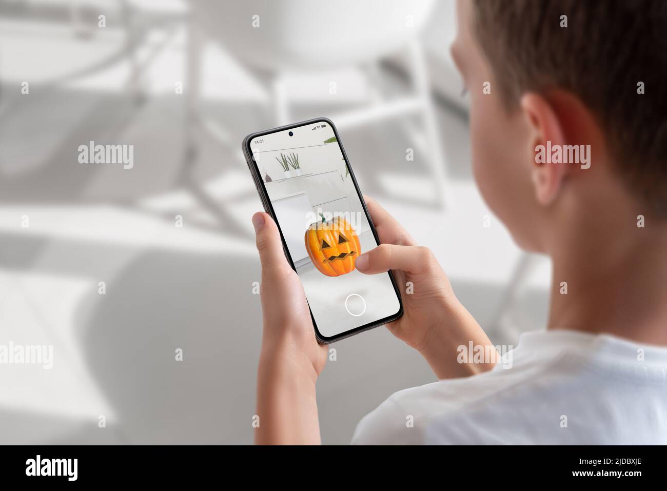 Boy on a mobile phone is playing an augmented reality game. View over shoulder at the phone display. Pumpkin throwing game concept Stock Photo
