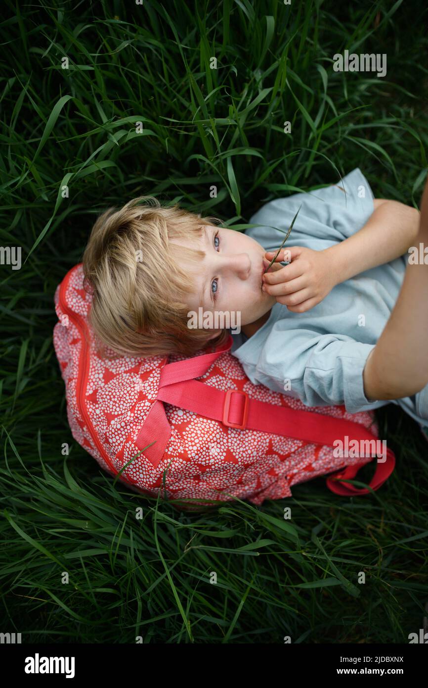 Happy first day of school. Tired schoolboy with backpack, lies on the grass. Stock Photo