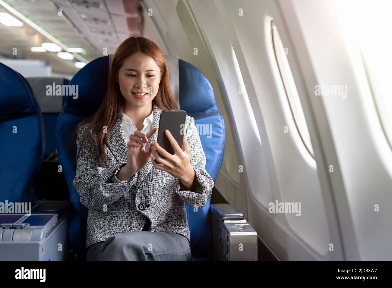 Travel and technology. Young asian woman in plane using smartphone while sitting in airplane seat Stock Photo