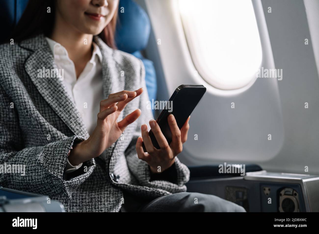Travel and technology. Young asian woman in plane using smartphone while sitting in airplane seat Stock Photo