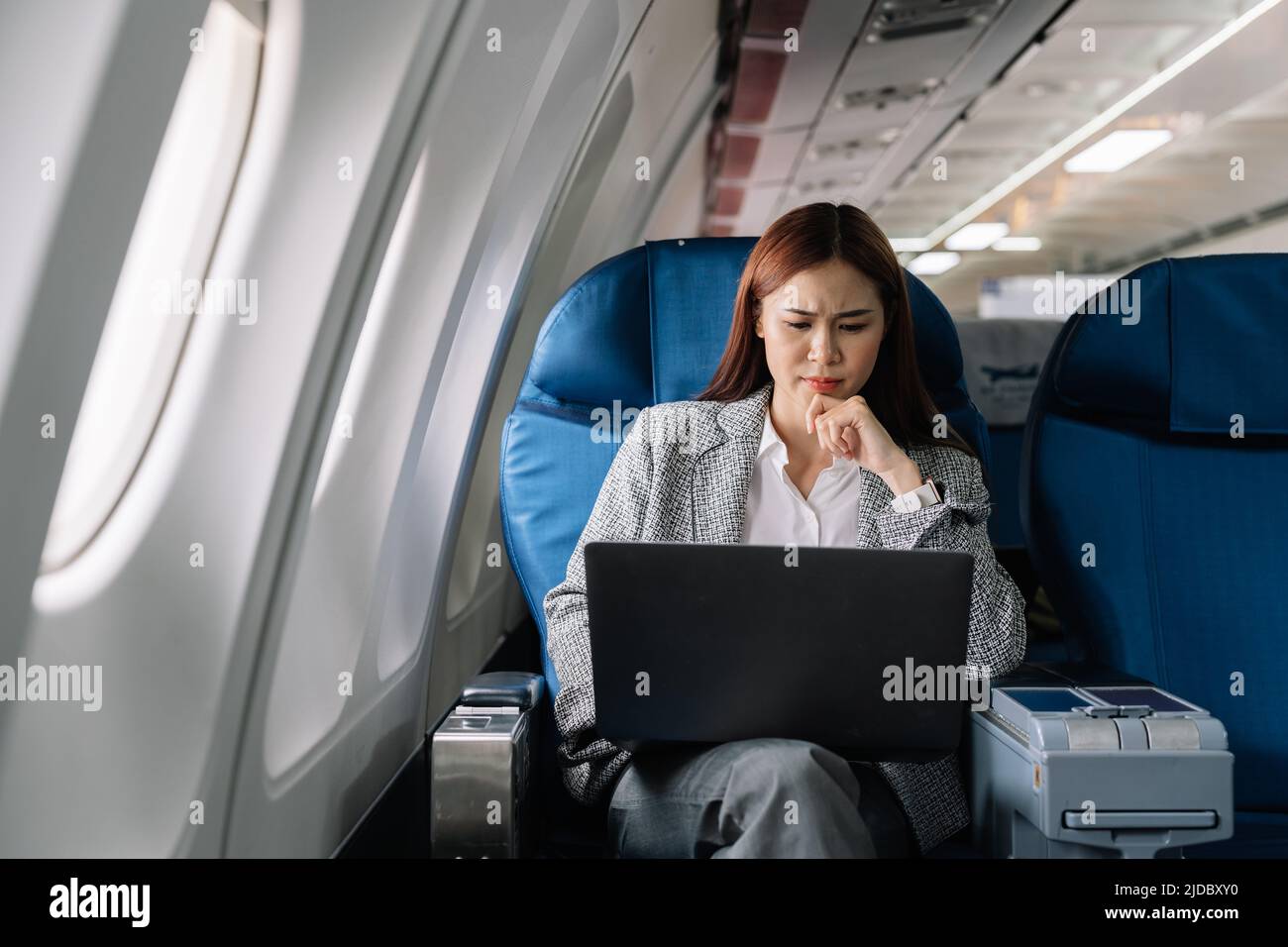serious asian young woman using laptop sitting near windows at first class on airplane during flight, Traveling and Business concept Stock Photo