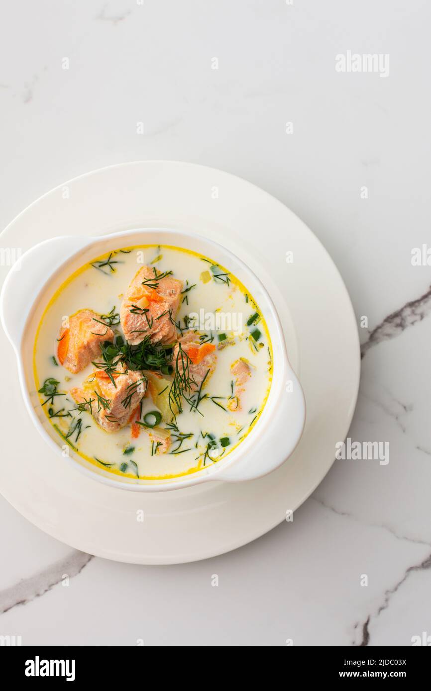 Norwegian red salmon fish soup with vegetables, herbs and cream, top view of a bowl of soup on a white marble background Stock Photo